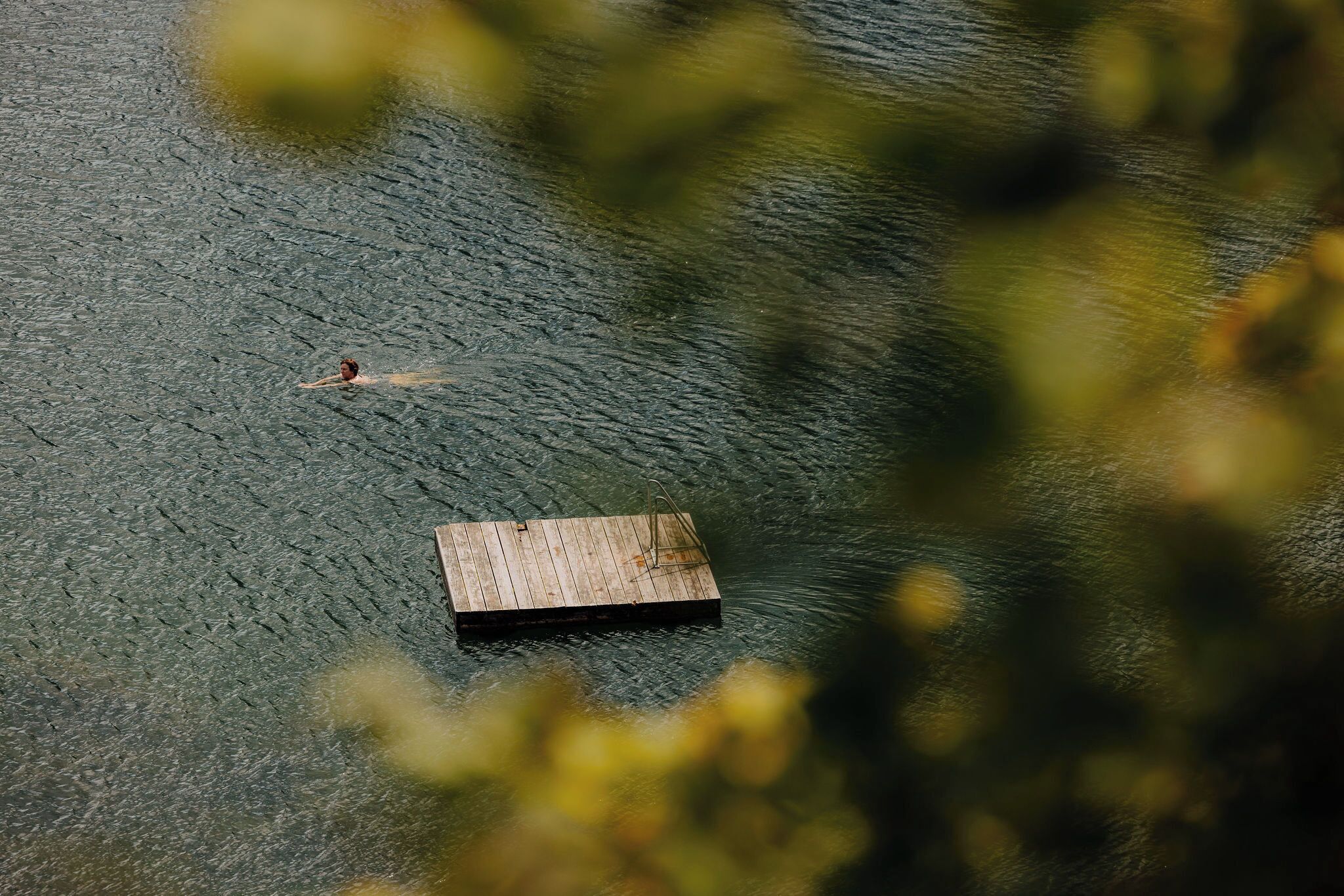 Eine Person schwimmt in einem Gewässer, im Vordergrund ein Holzsteg.