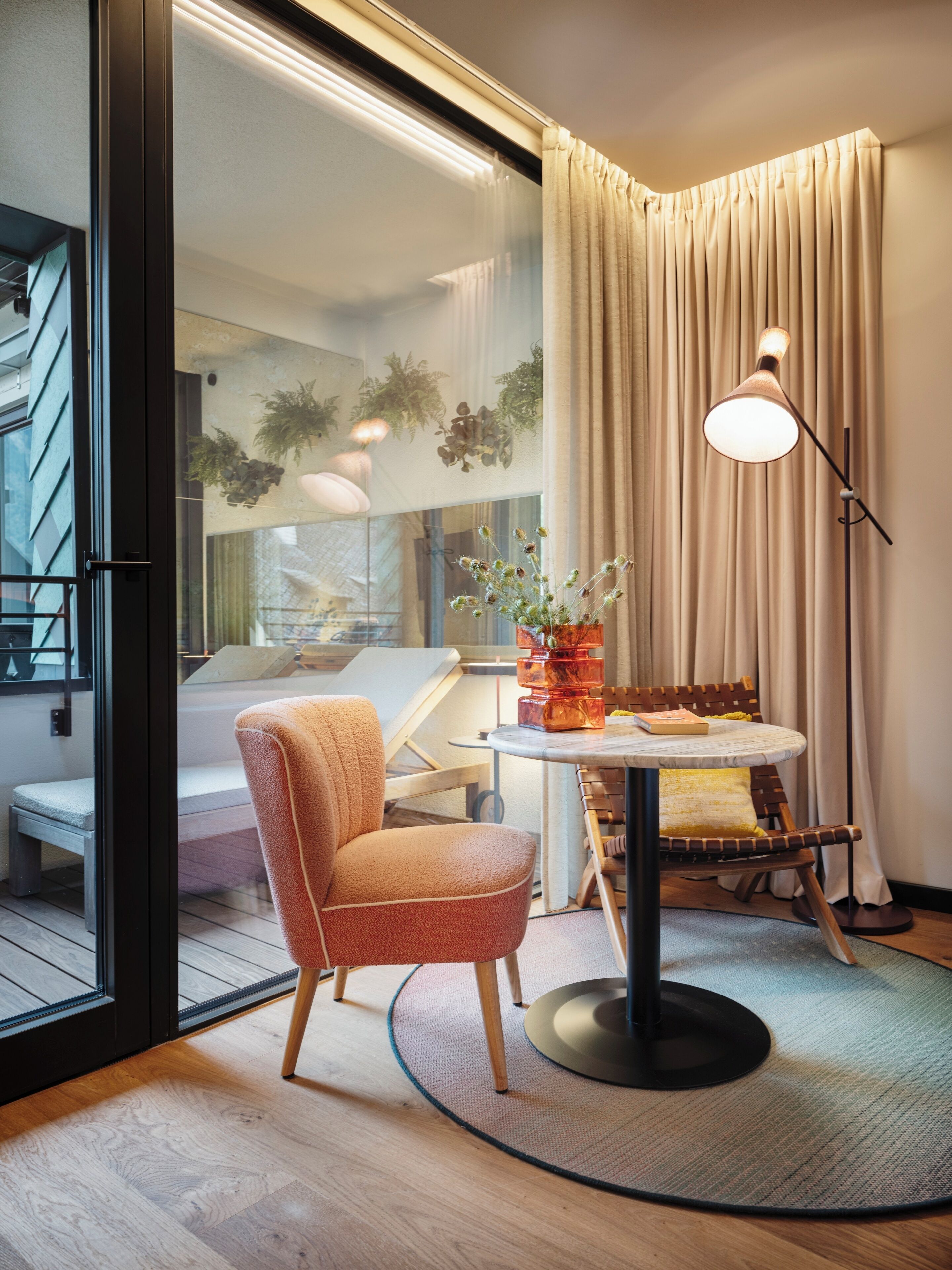 Ein modernes Zimmer mit rundem Tisch, einem Stuhl, einer Stehlampe und Blick auf einen Balkon.
