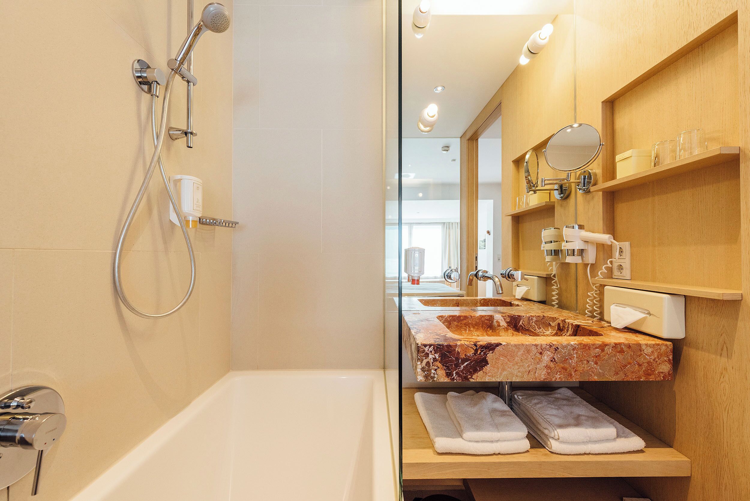 Un baño moderno con bañera, ducha con cabezal de ducha manual, lavamanos de mármol y tocador con espejo y toallero.