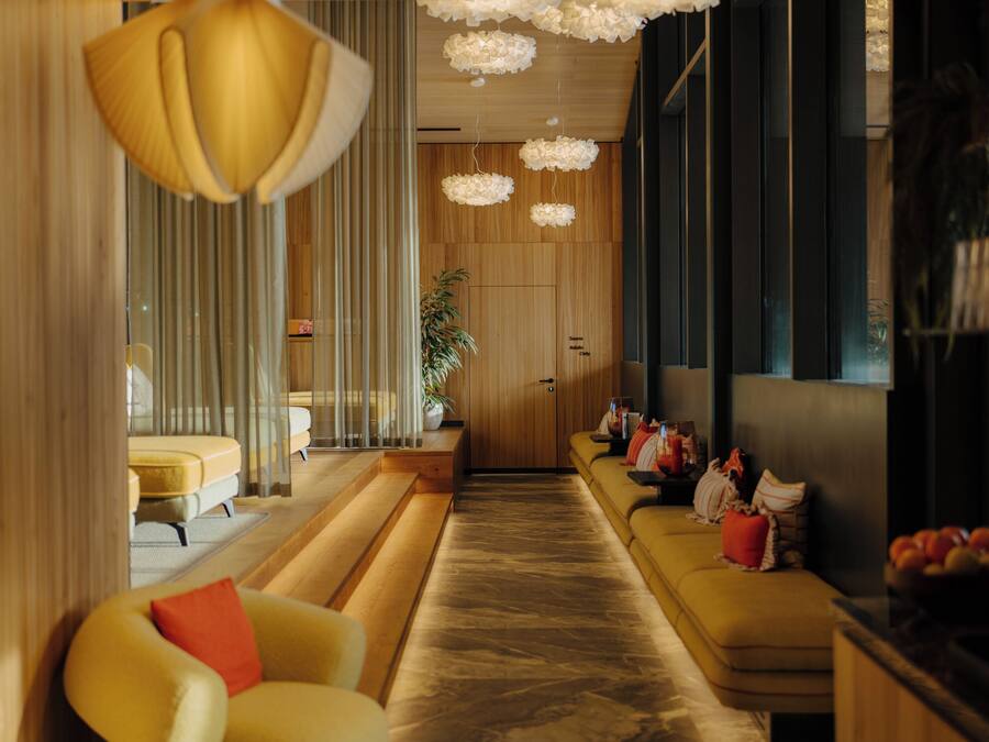 Un vestíbulo de hotel moderno con un mostrador de recepción alargado, sofás amarillos y una planta grande en maceta.