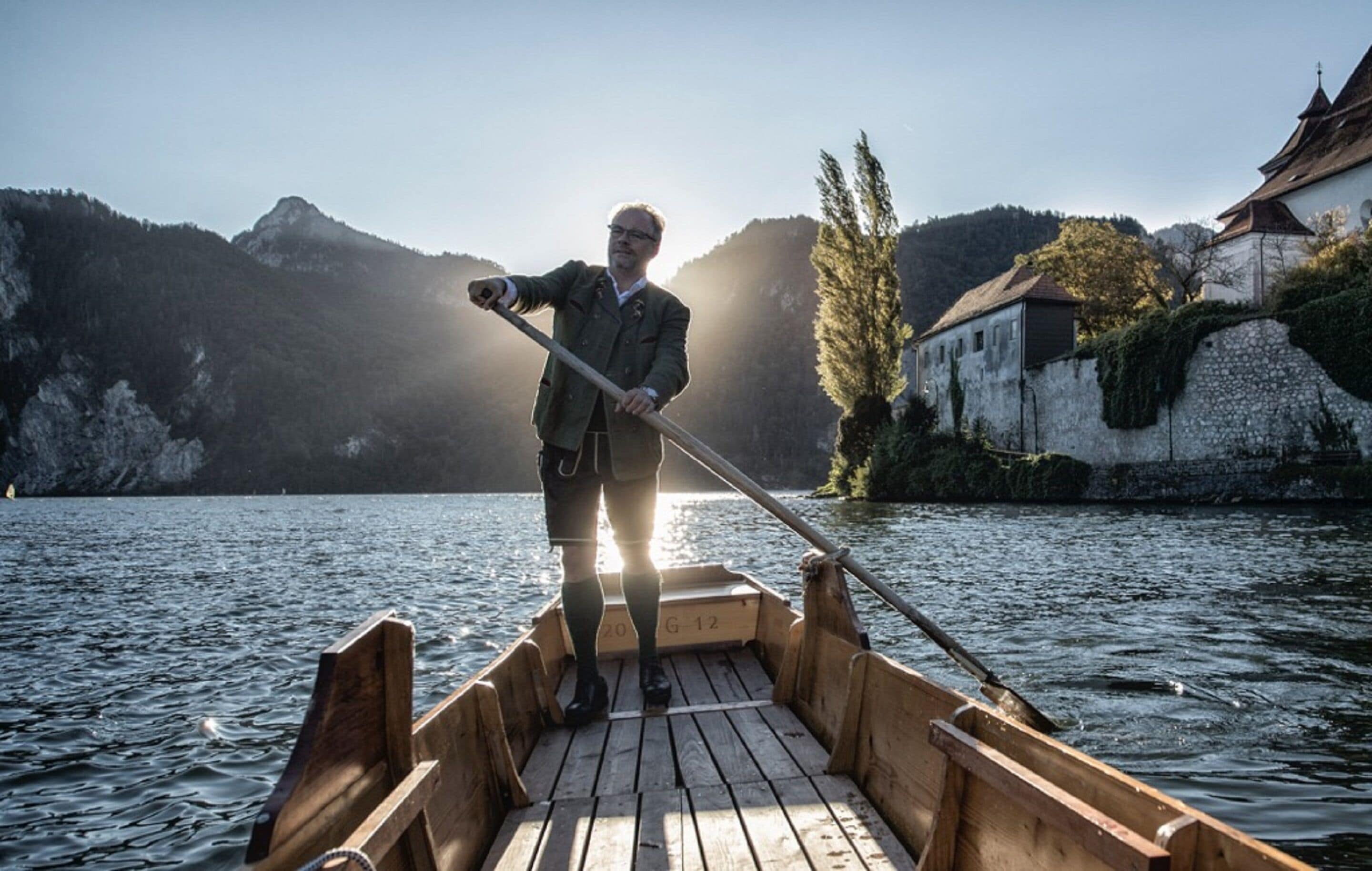 Ein hölzernes Boot auf ruhigem Wasser, eine Person steht vorne und hält eine Stange.