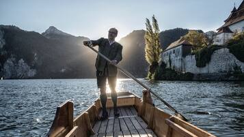 Ein hölzernes Boot auf ruhigem Wasser, eine Person steht vorne und hält eine Stange.