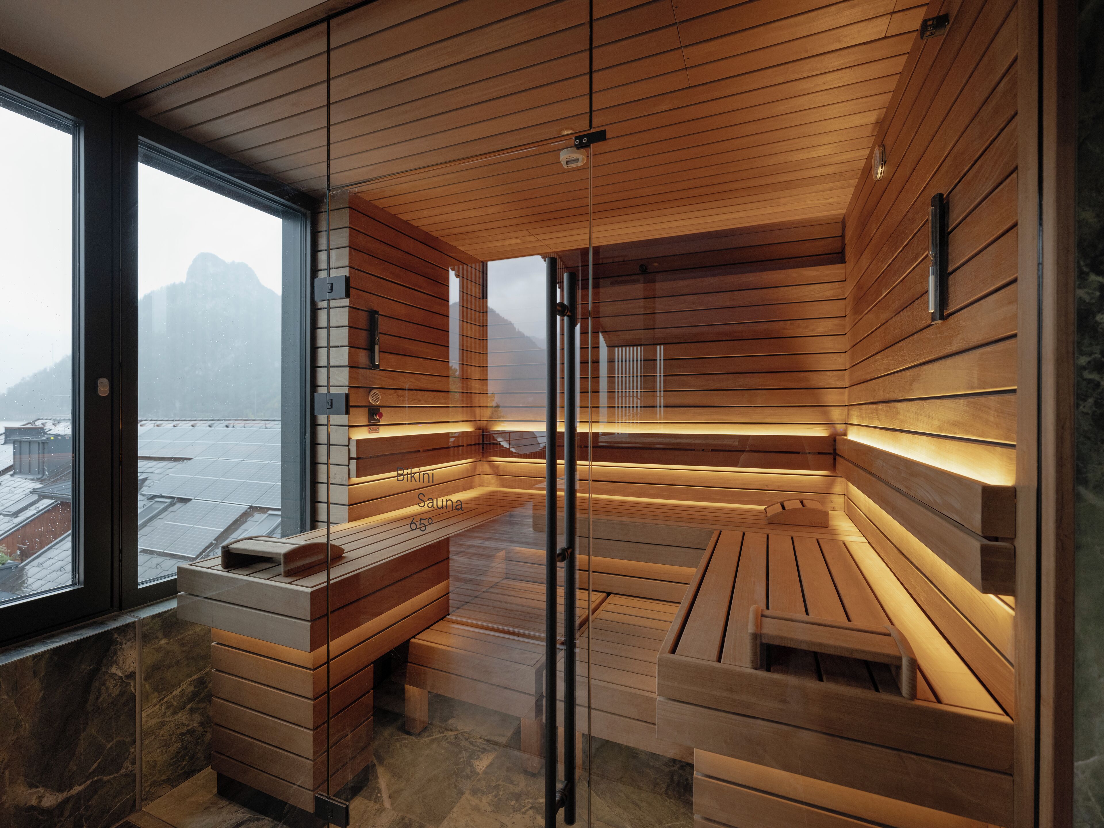 Una sauna con bancos de madera y una pared de vidrio que ofrece vistas a un paisaje nevado.