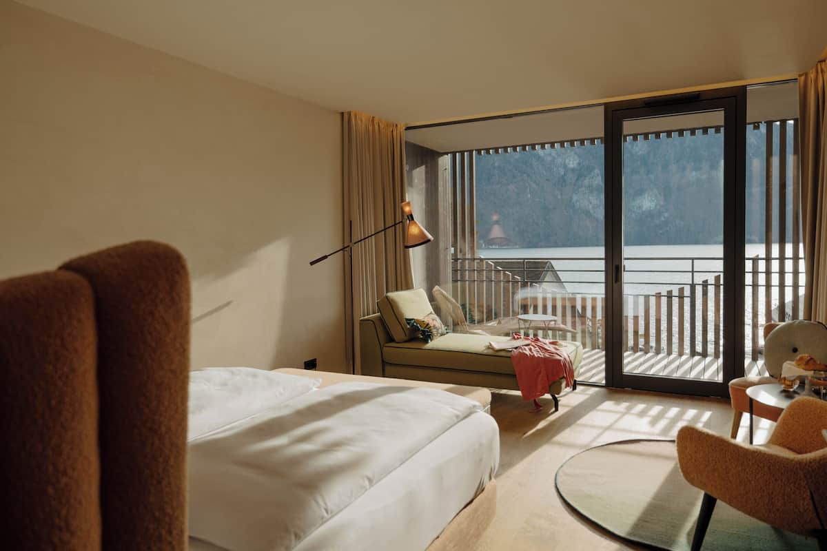 A hotel room with a bed, a sofa, a chair, a table, and a balcony with a view of the sea.