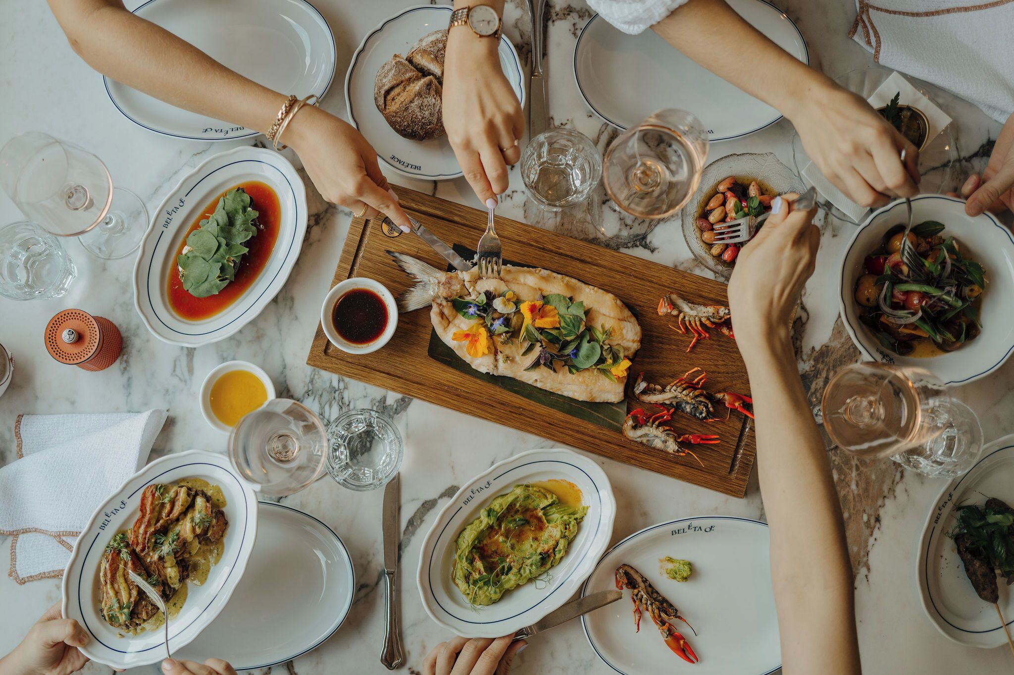 A dining table with multiple plates of food, glasses of water, and cutlery.