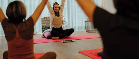 A yoga class in a room with a wooden floor, yoga mats, and a small table with a bowl of snacks.