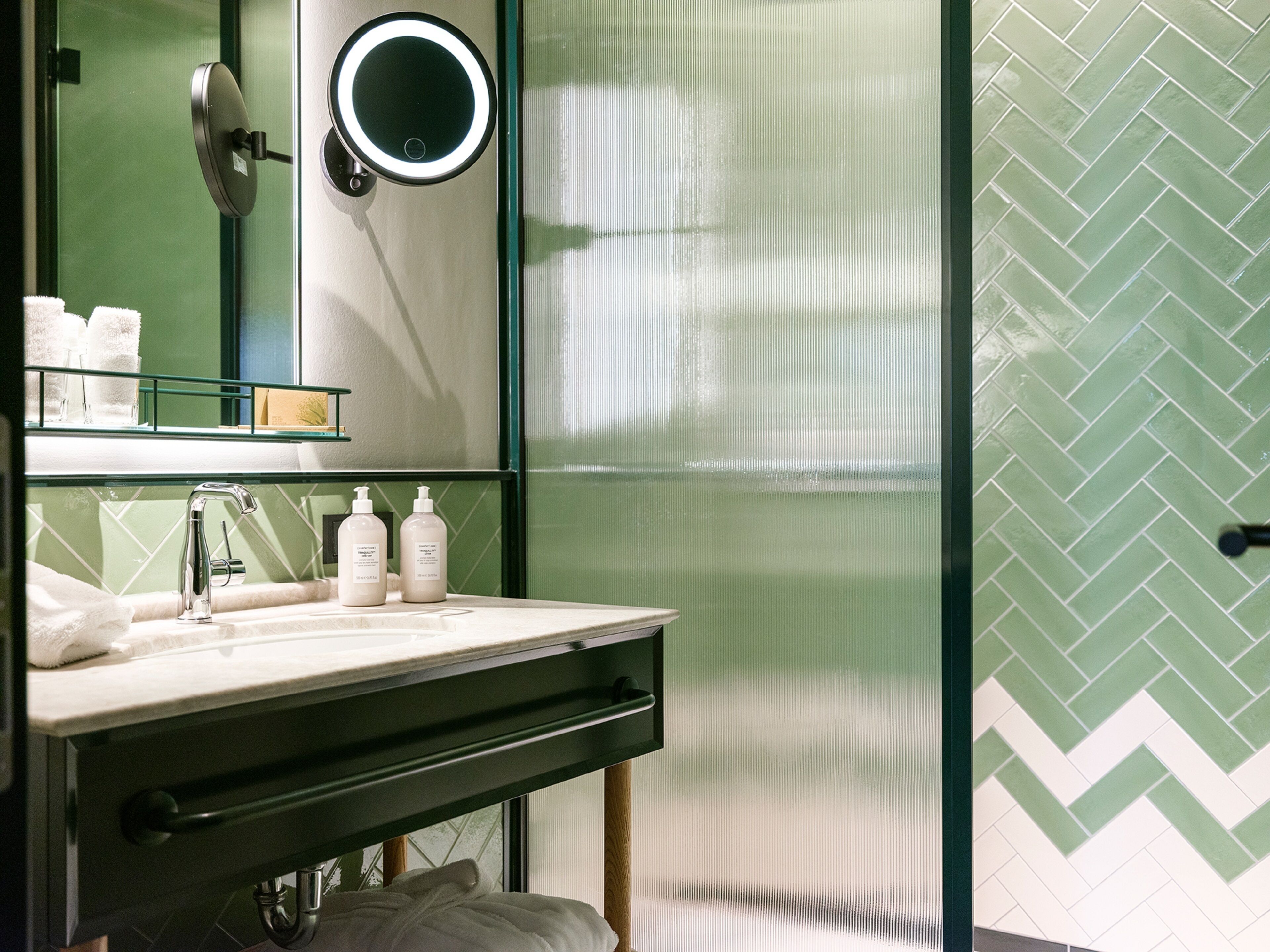 A modern bathroom with a glass-enclosed shower, a vanity with a mirror, and a green herringbone-patterned wall.