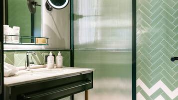 A modern bathroom with a glass-enclosed shower, a vanity with a mirror, and a green herringbone-patterned wall.