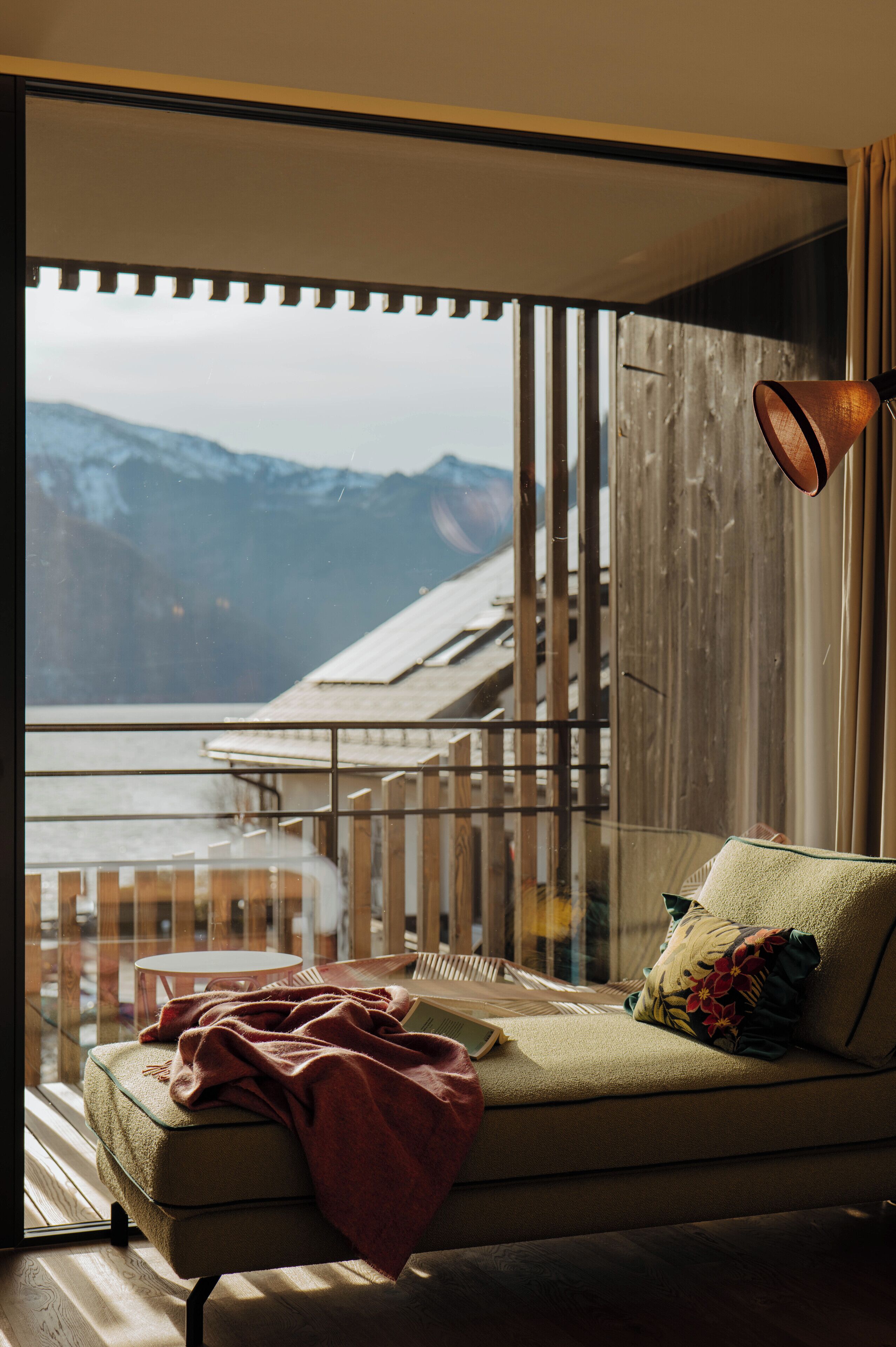 A modern living room with a view of mountains, a sofa, a lamp, and a glass partition.
