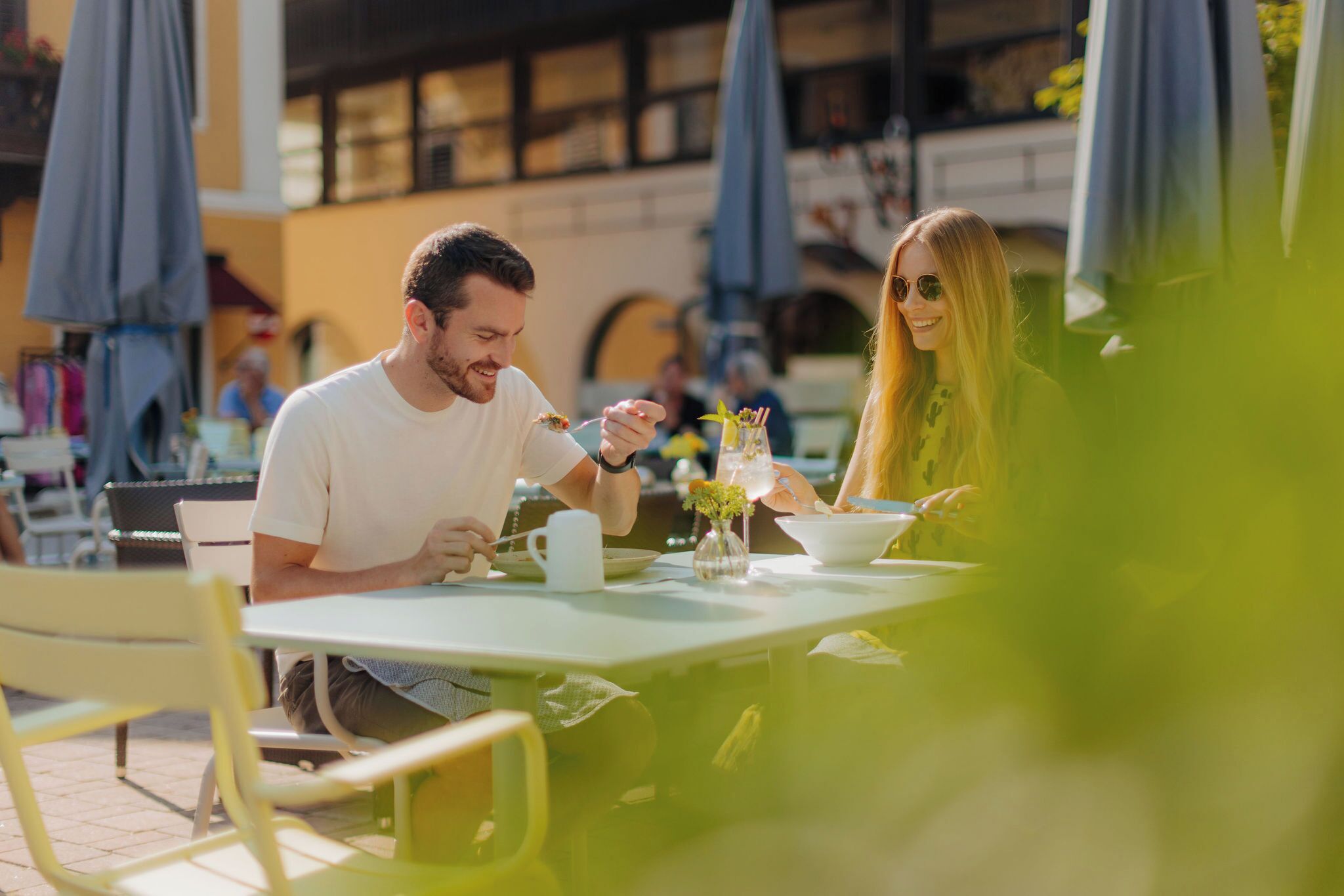 A couple dining at an outdoor café with tables and umbrellas.