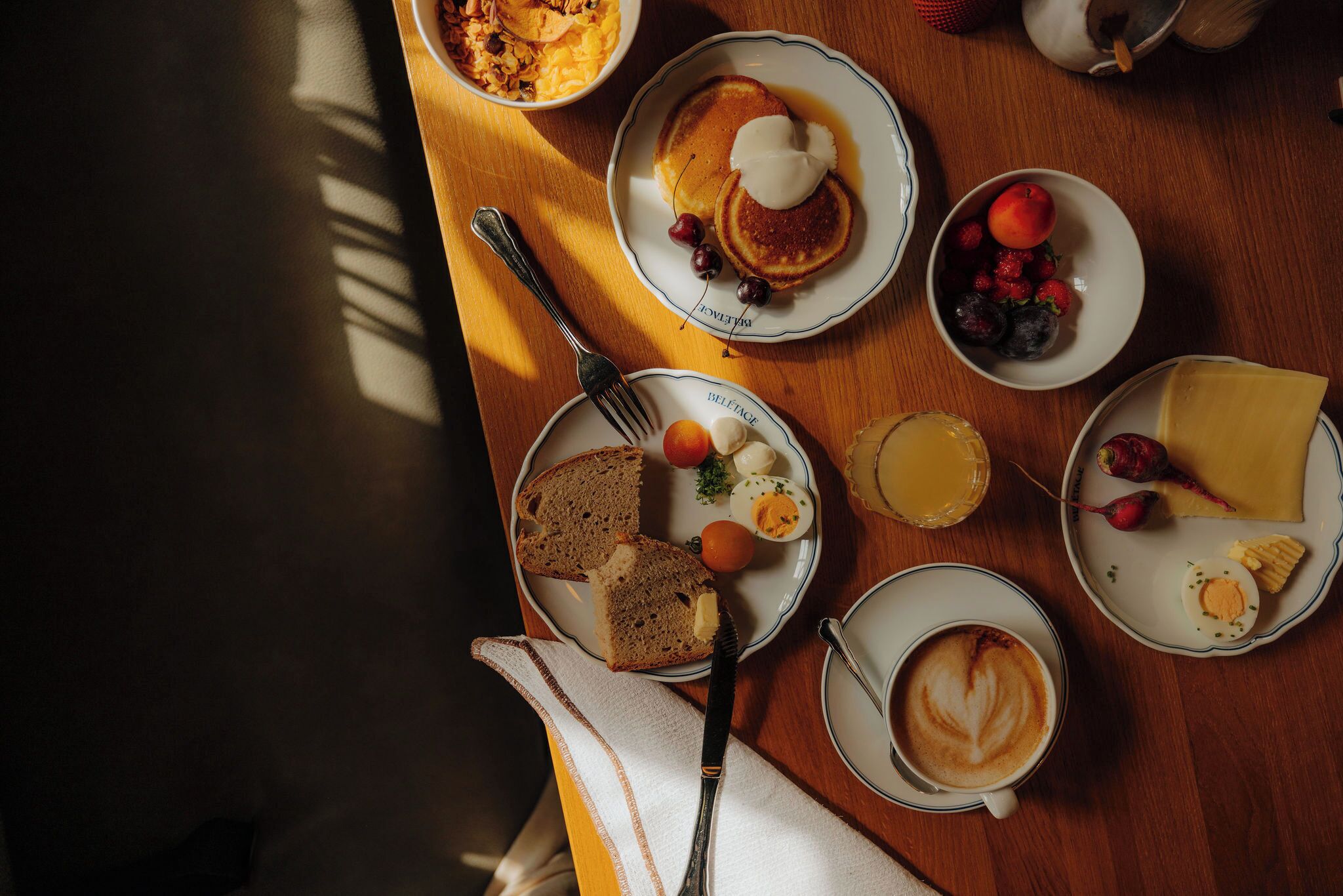 Een ontbijt met pannenkoeken, eieren, toast, fruit, kaas en koffie op een houten tafel.