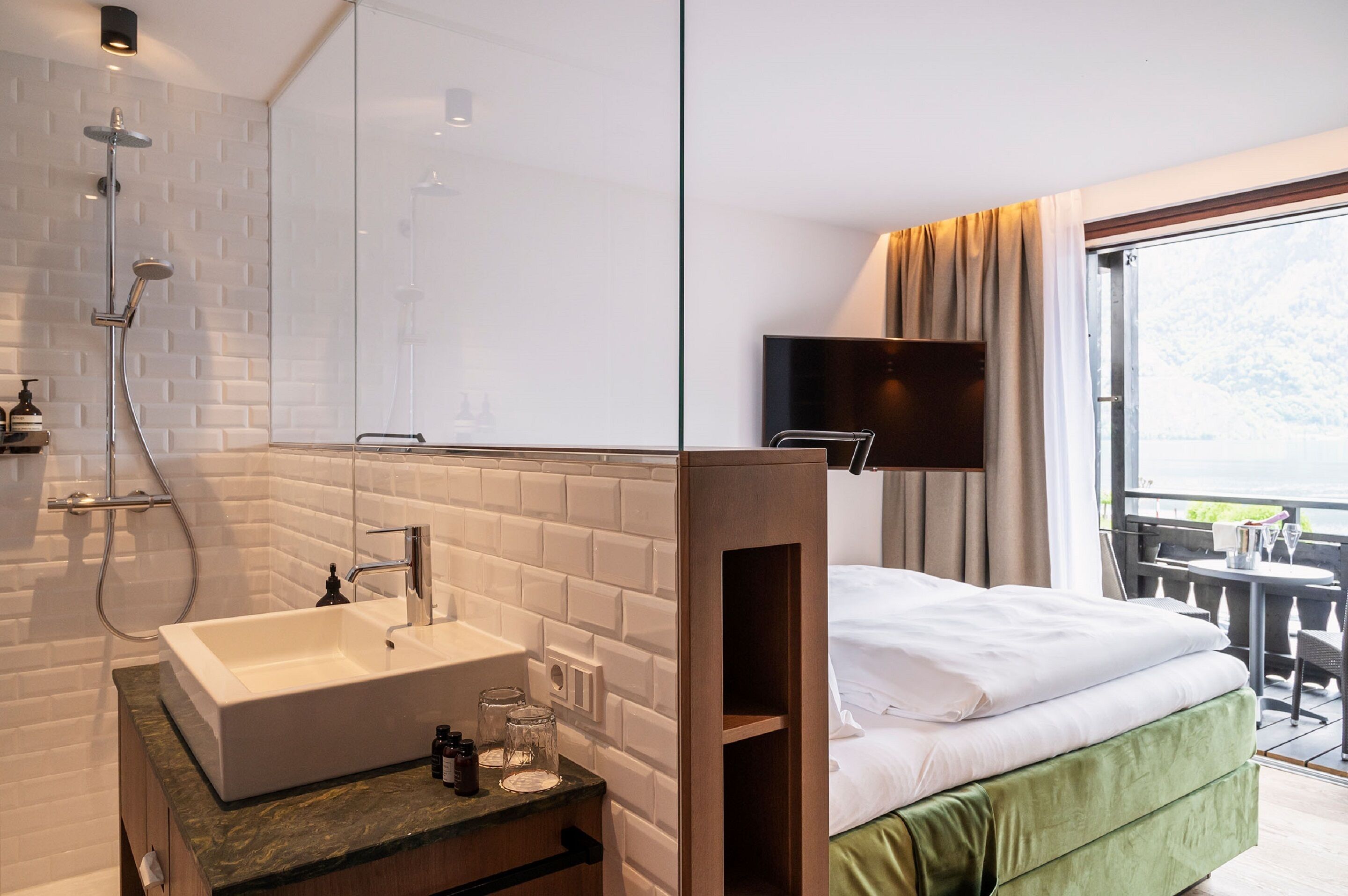 Ein Hotelzimmer mit großem Fenster, Dusche, Waschbecken, Bett und Fernseher.