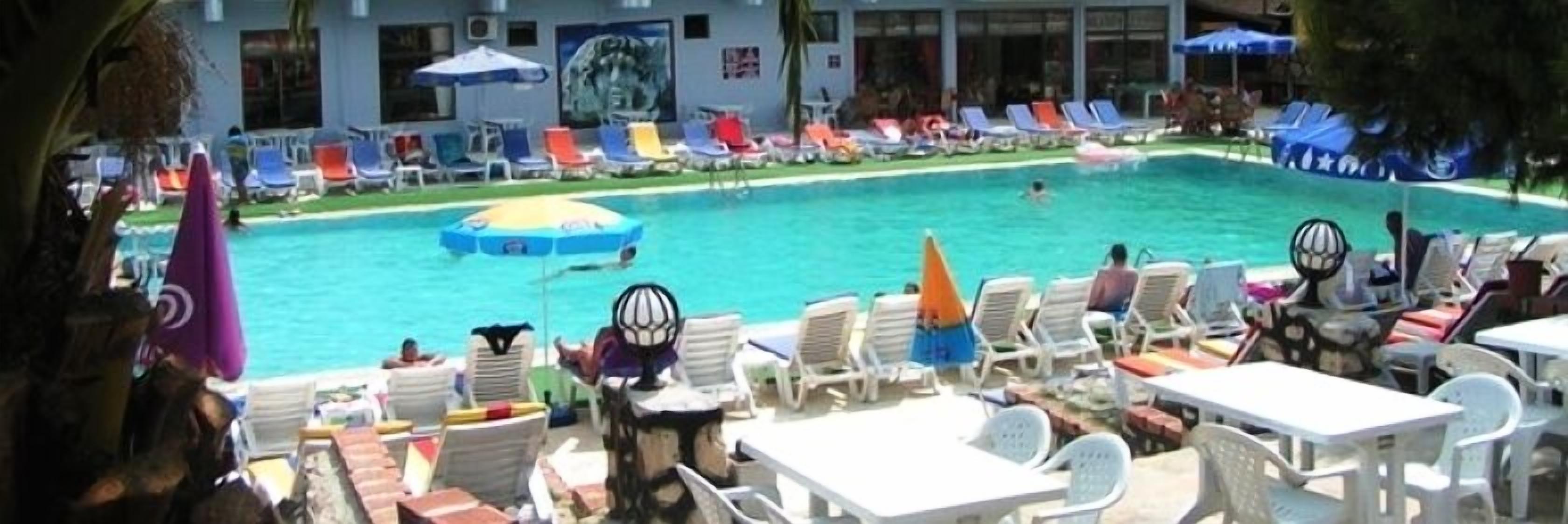A poolside area with lounge chairs and umbrellas, a swimming pool, and a building with a mural in the background.