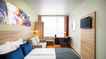 Una habitación de hotel con cama, escritorio, silla, televisor y un cuadro abstracto grande en la pared.