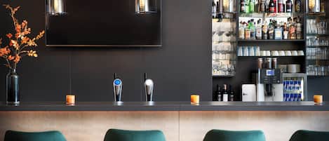 A bar area with a flat-screen TV, two pendant lights, a bar counter, and a shelf with various bottles and glasses.