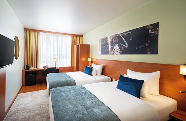 A hotel room with two beds, a desk, a TV, and a large window with curtains. - Leonardo Hotel Salzburg Airport (Wals-Siezenheim)