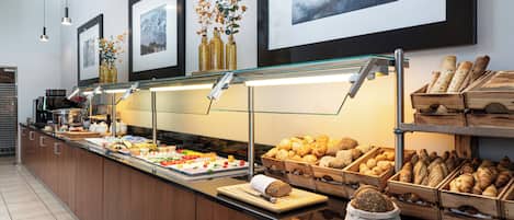Un área de buffet con diferentes opciones de comida, incluyendo pan y bollería, y cuadros en la pared.