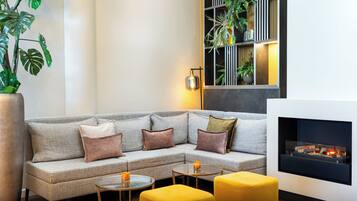 Un salon moderne avec un canapé gris, un pouf jaune et une cheminée.