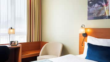 A hotel room with a bed, a desk with a lamp, a chair, and a wall-mounted TV.