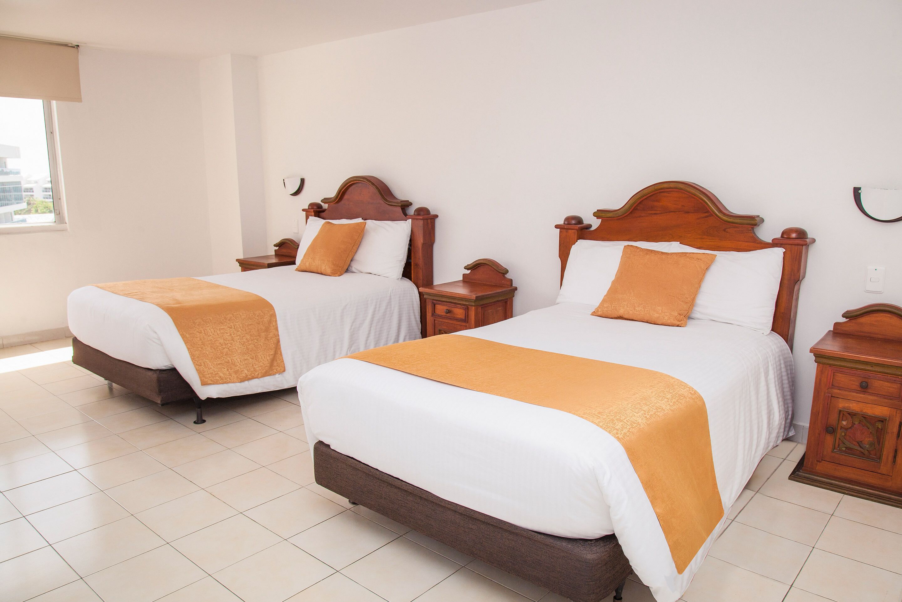 Two double beds with wooden headboards, white bedding, and orange throw blankets.