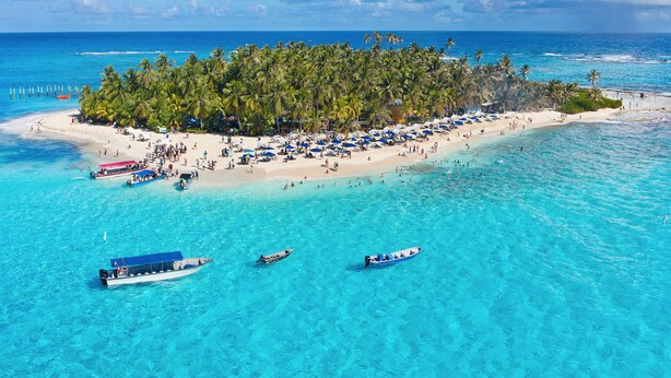 A tropical island beach with clear turquoise waters, palm trees, and beach umbrellas. - Sol Caribe Sea Flower (San Andrés)