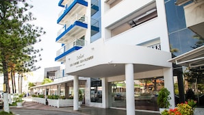 A modern building with a white and blue facade, a covered entrance area, and potted plants. - Sol Caribe Sea Flower (San Andrés)