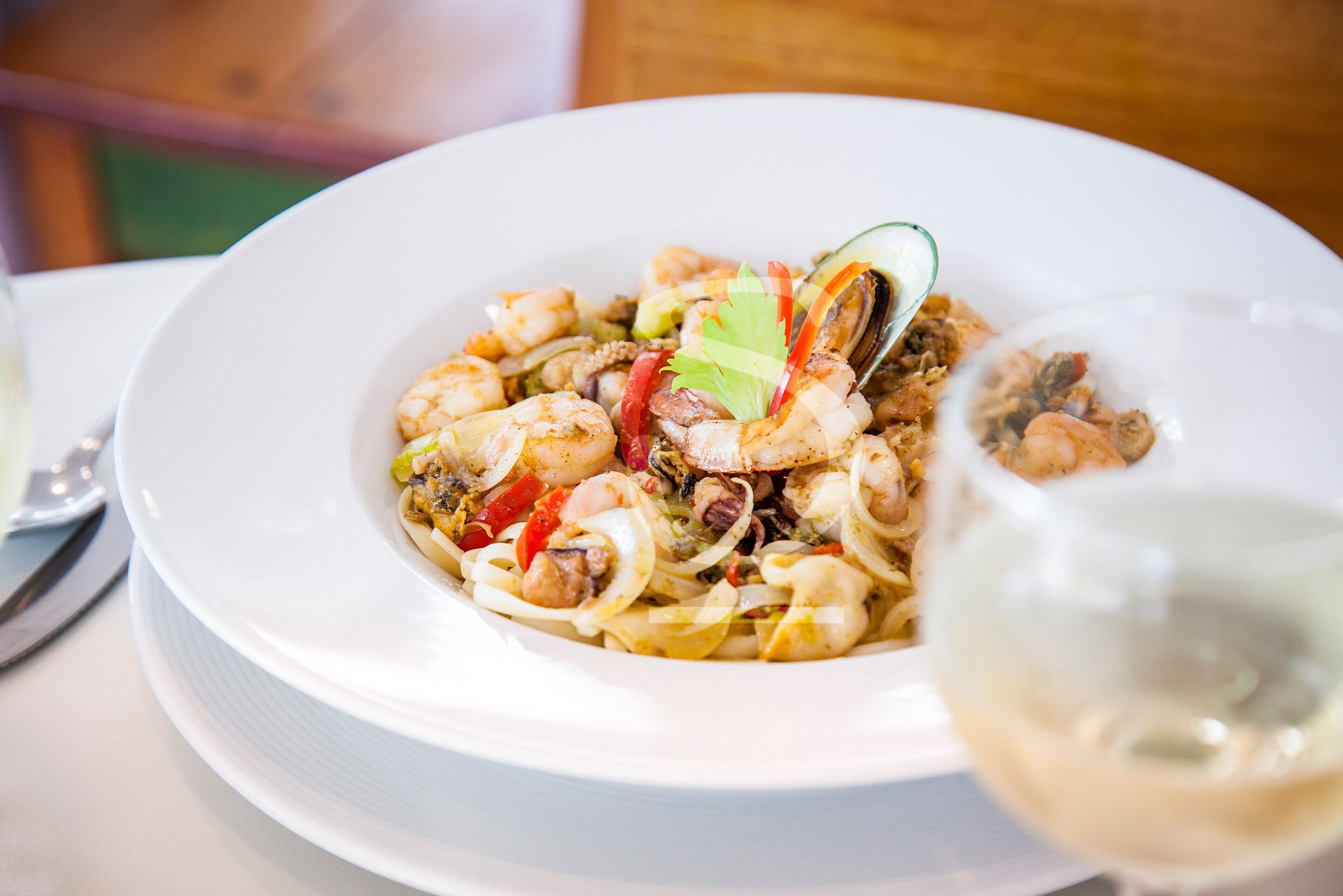 A plate of seafood pasta with a glass of white wine on the table.