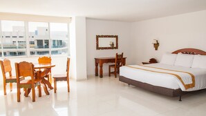 A hotel room with a bed, a desk, a chair, a mirror, and a window with a view of buildings. - Sol Caribe Sea Flower (San Andrés)
