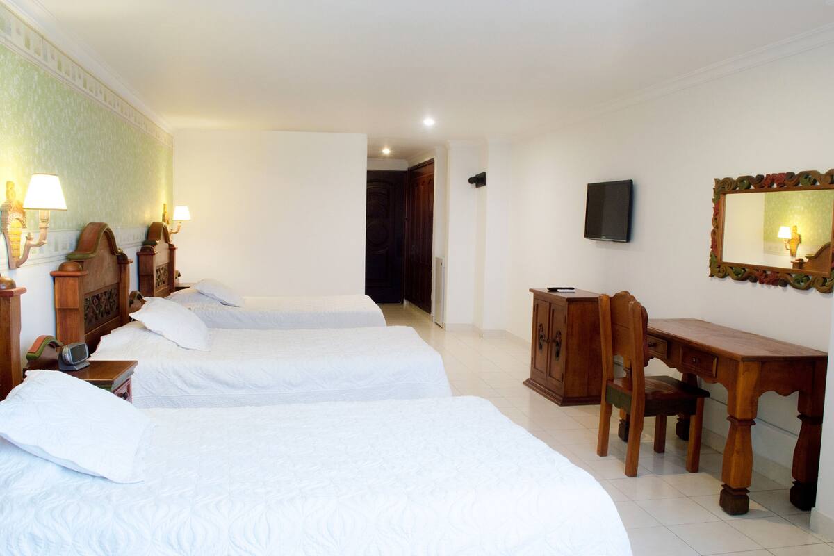 A hotel room with two beds, a wooden desk, a television, and a mirror.