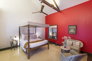 Una cama con dosel, un cabecero rojo, un sofá y una mesita con flores.