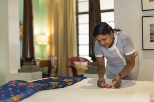 Una persona en una habitación con una cama, un edredón estampado y una lámpara al fondo.