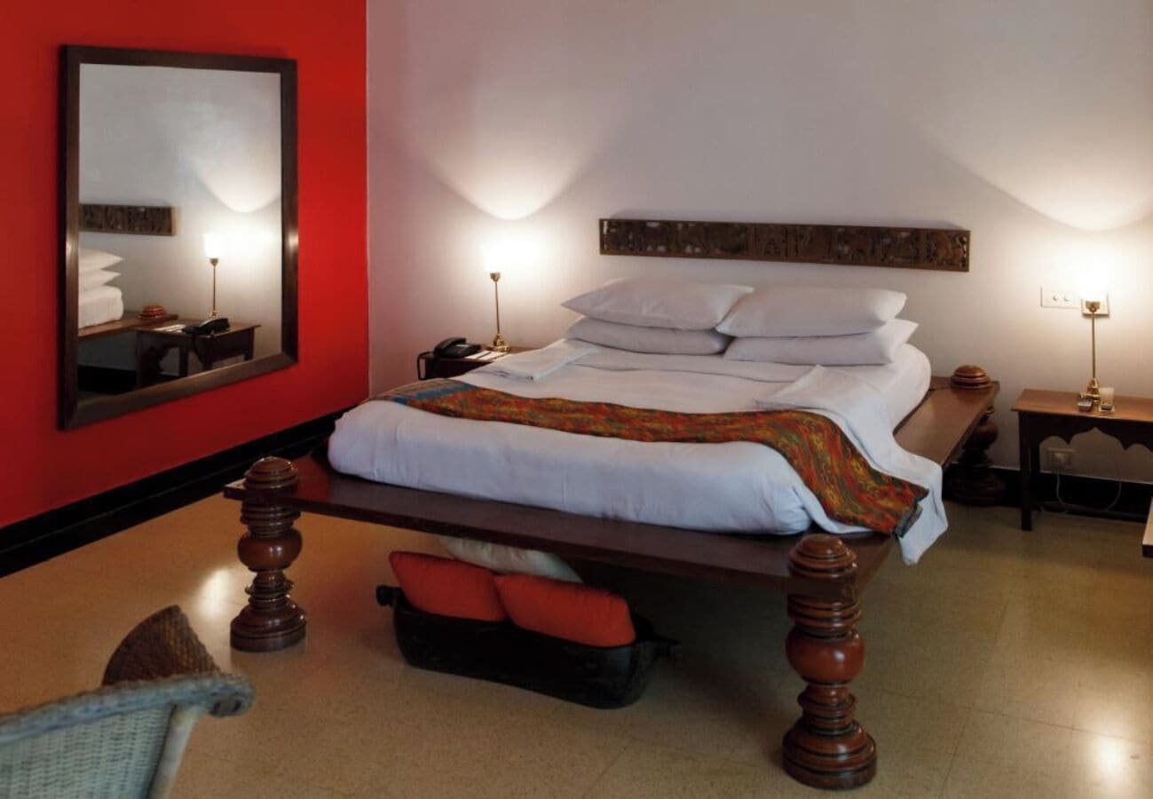 A hotel room with a bed, bedside tables, a mirror, and a red wall.