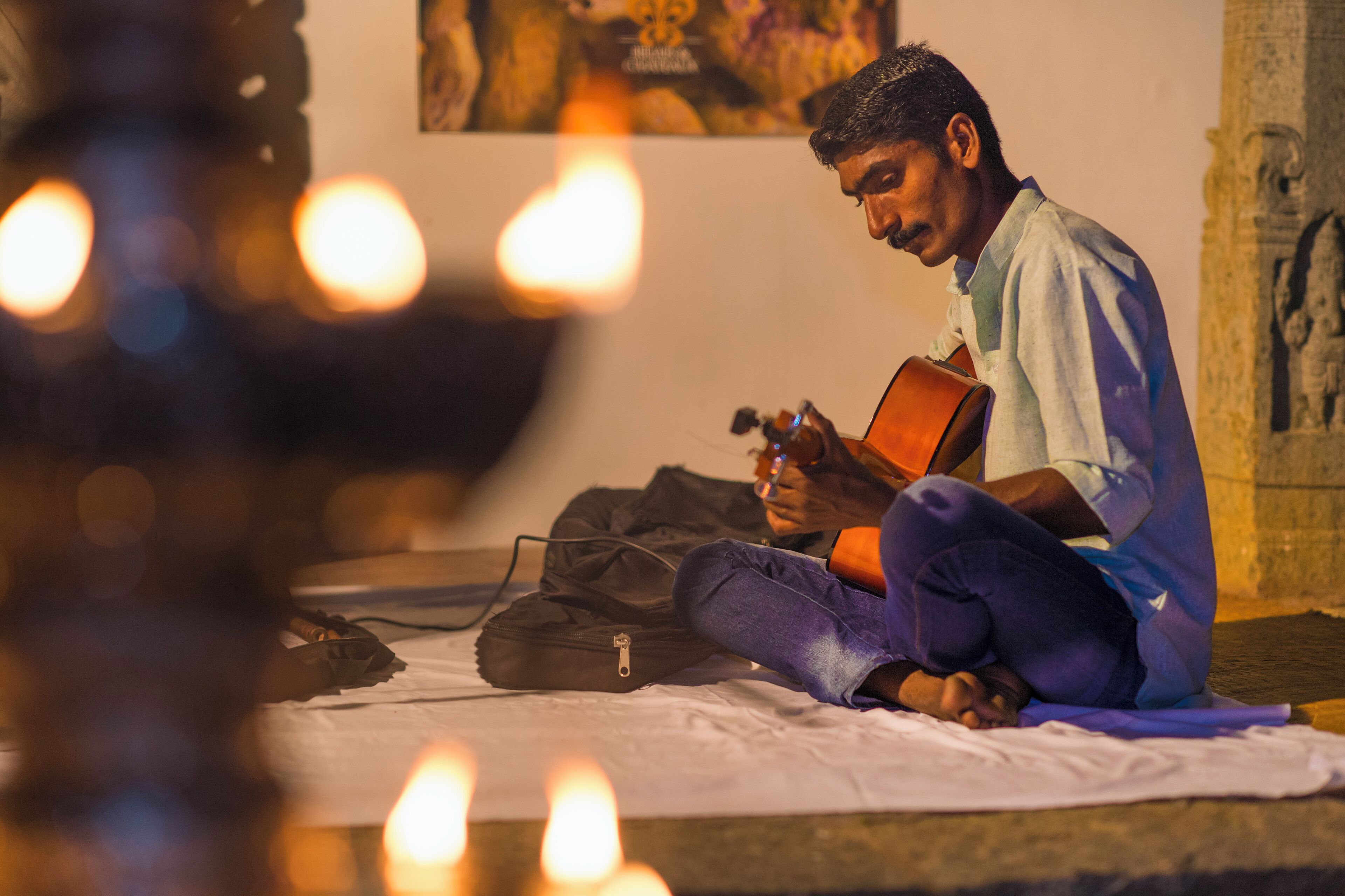 A person sitting on a bed with a guitar, surrounded by lit candles.
