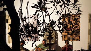 Una habitación con piso reflectante, una mesa con sillas y una persona tocando la guitarra.