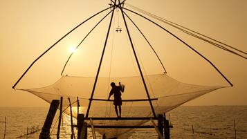 Una persona de pie bajo una gran estructura de red de pesca al atardecer.