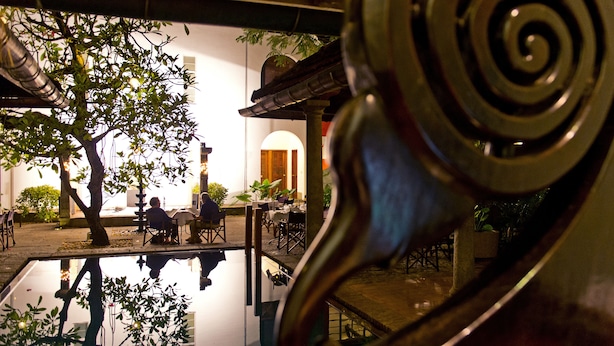 Un patio con un estanque reflectante, un árbol y un edificio con un arco de entrada.