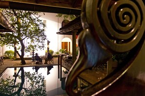 A courtyard with a reflective pool, a tree, and a building with an arched doorway. - The Malabar House (Kochi)