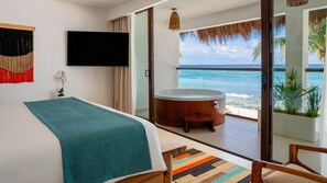 A hotel room with a bed, a TV, a balcony with a hot tub, and a view of the ocean.