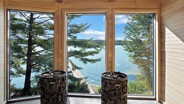 Habitación con ventanas amplias que ofrecen vista a un lago y árboles. Hay dos macetas de piedra en el alféizar.