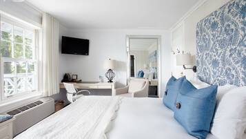Quarto de hotel com uma cama grande, uma escrivaninha com cadeira, televisão e banheiro visível por uma porta aberta.
