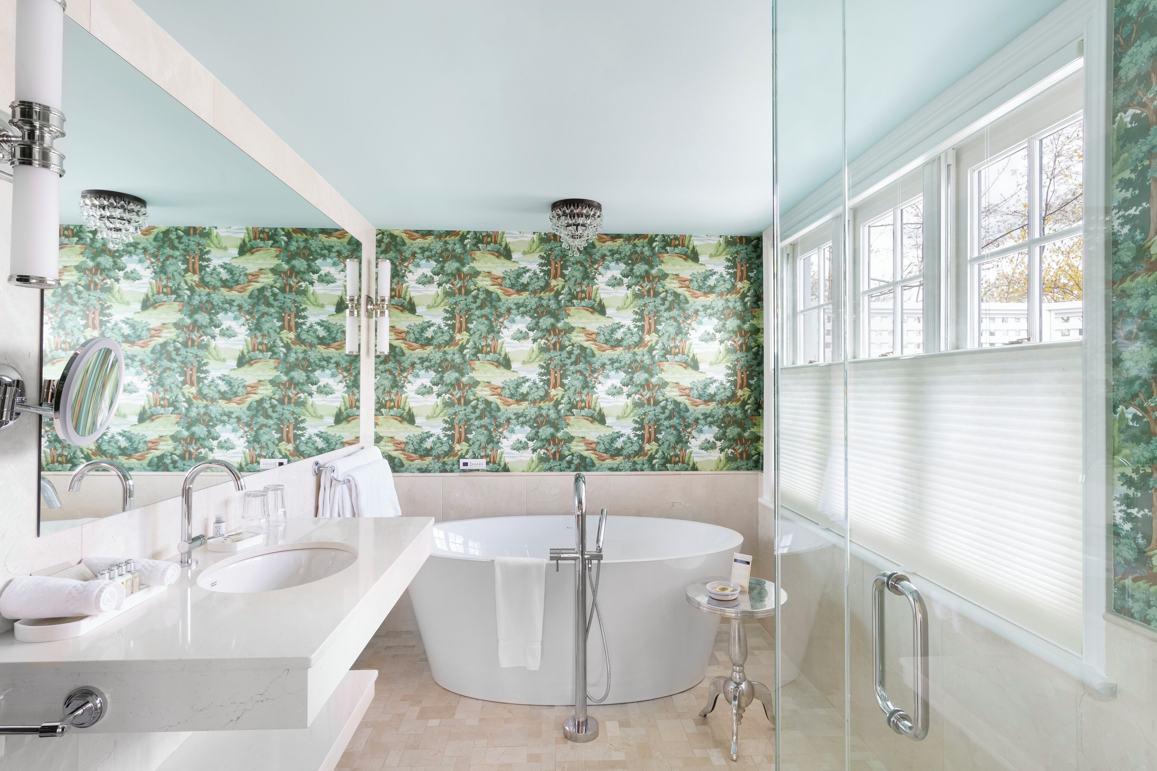 Une salle de bain moderne avec une baignoire sur pieds, un meuble-lavabo avec un miroir et une grande fenêtre équipée de stores.