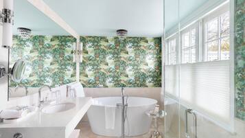 Une salle de bain moderne avec une baignoire sur pieds, un meuble-lavabo avec un miroir et une grande fenêtre équipée de stores.