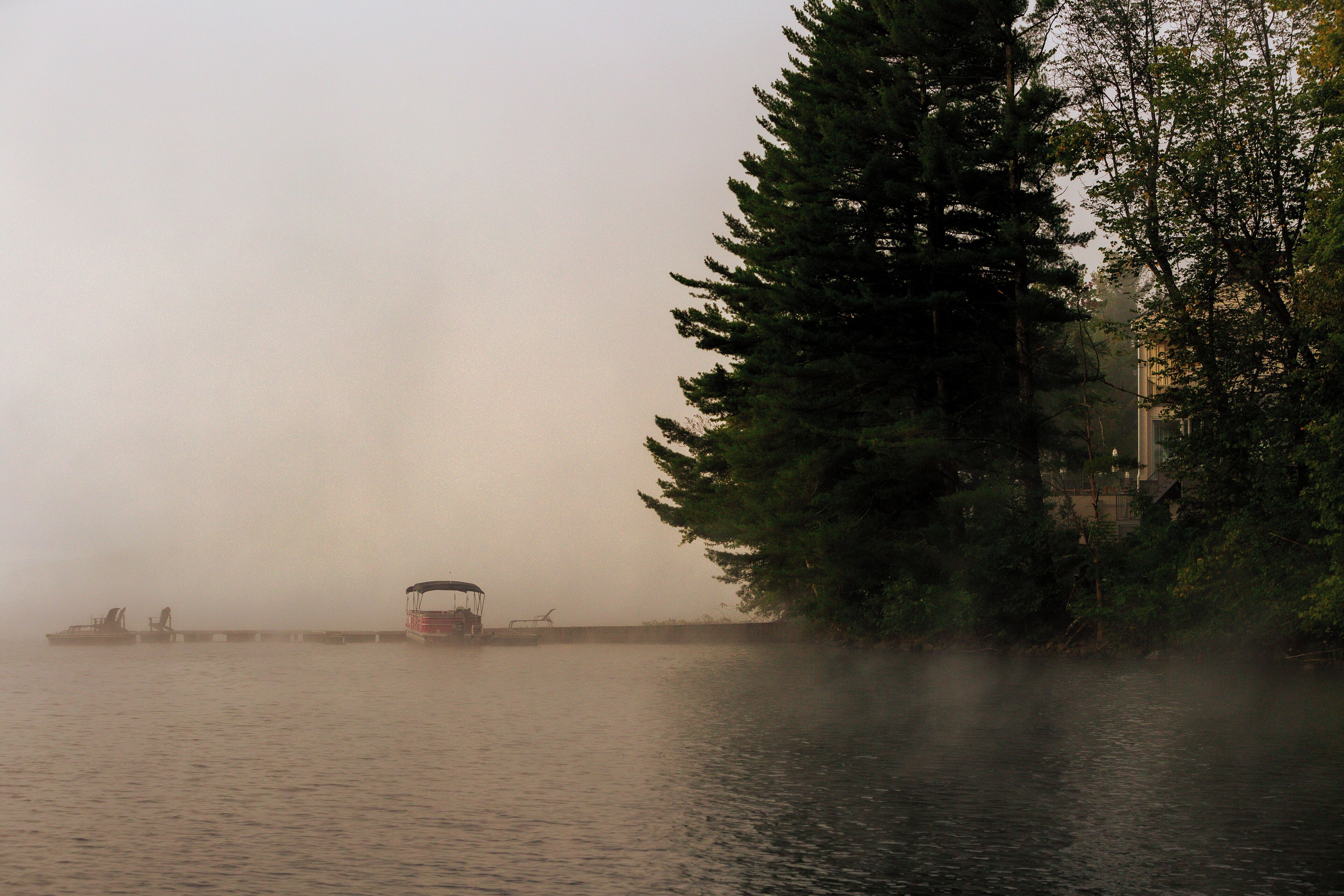 A foggy river scene with boats and a forested area.