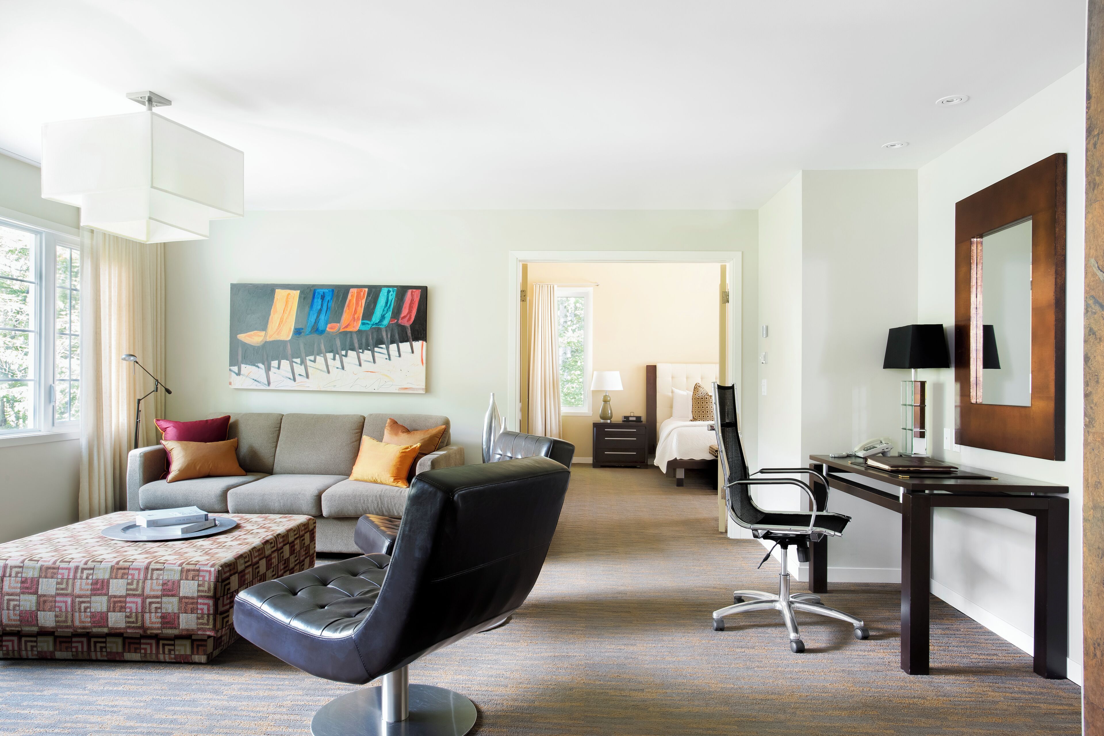 A modern hotel room with a sofa, a black office chair, a desk, and a large painting on the wall.