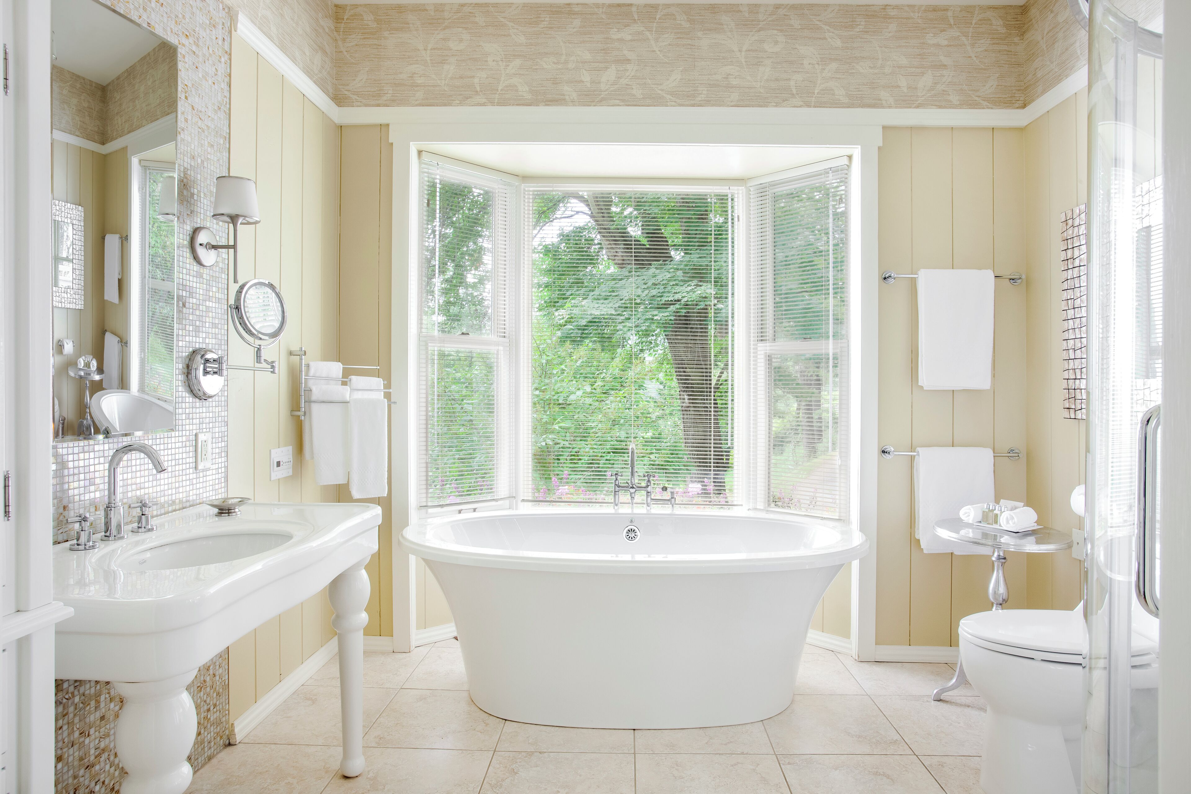 Un baño con una bañera independiente, un tocador con espejo y una ventana con persianas.