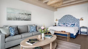 A modern bedroom with a grey sofa, a round wooden coffee table, a bed with a blue floral headboard, and a large abstract painting on the wall.
