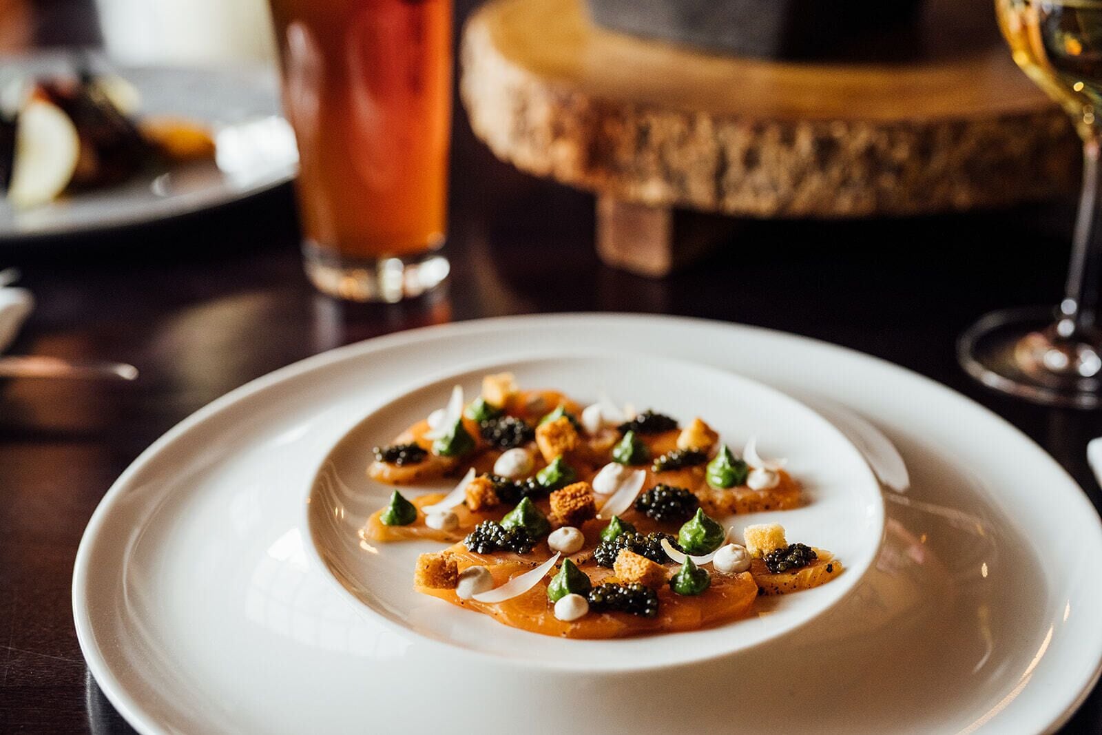 A white plate with a dish of food, a glass of red drink, and a wooden table.