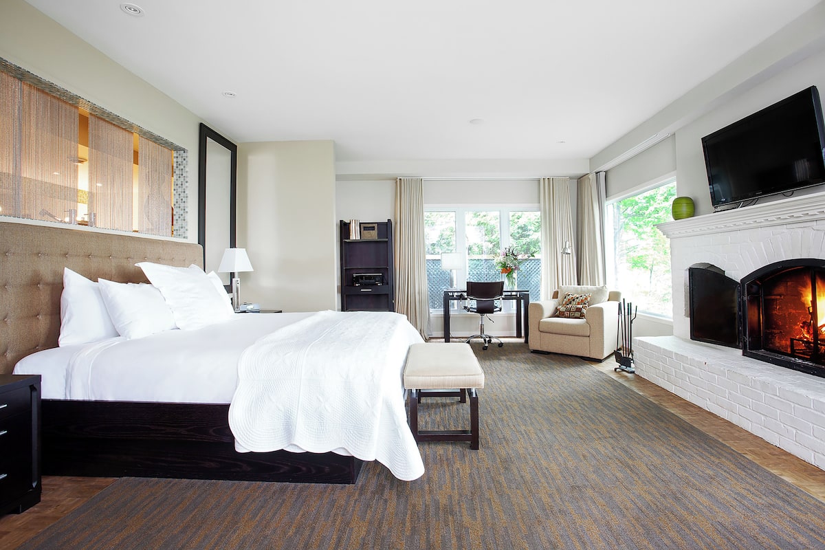 Quarto de hotel com uma cama grande, televisão, lareira e vista para o exterior.