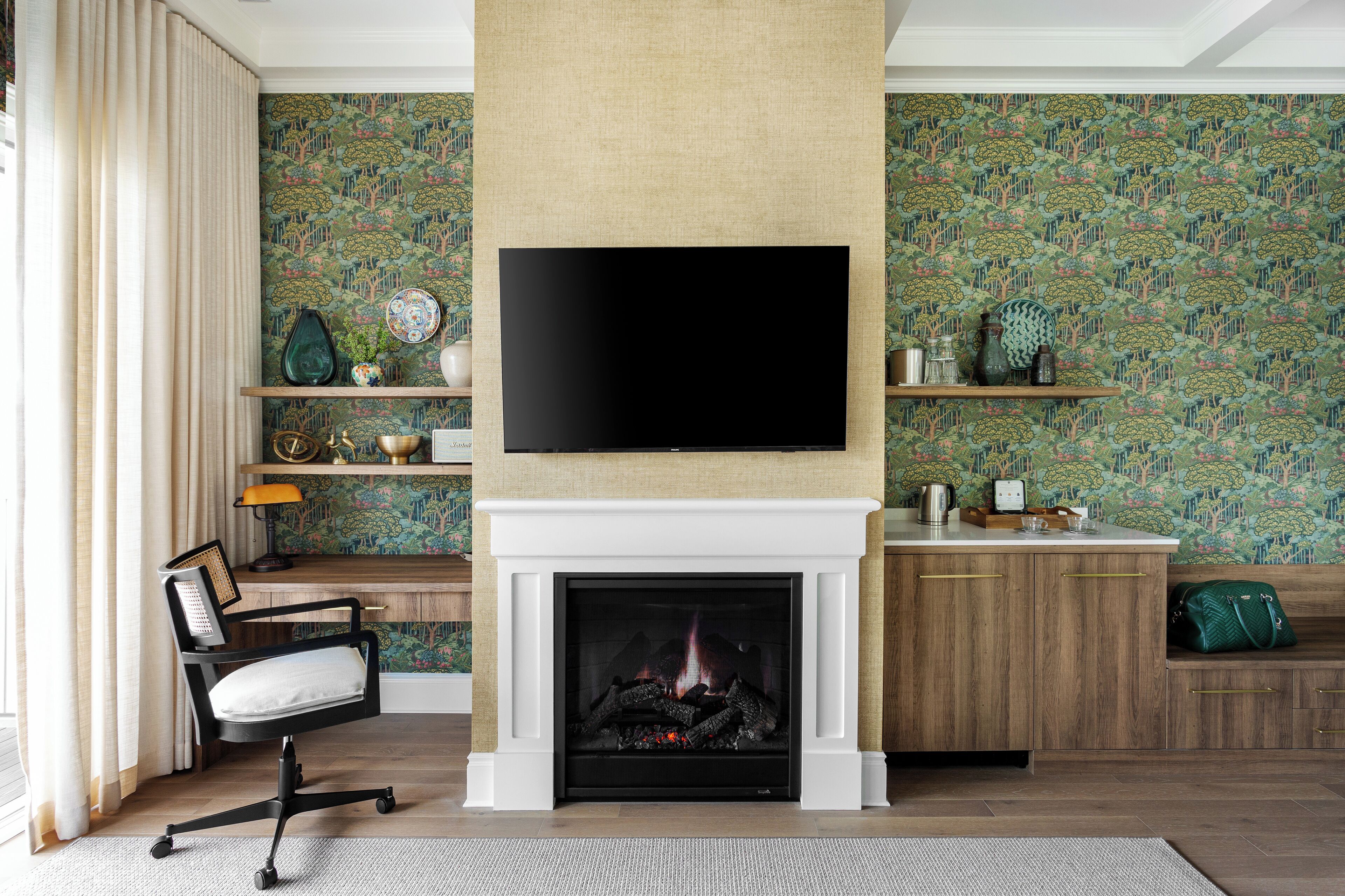 A living room with a fireplace, a television mounted above it, and patterned wallpaper.