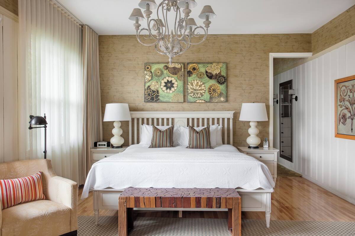 Quarto com uma cama grande, duas mesas de cabeceira, um candelabro e duas obras de arte florais na parede.